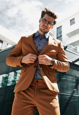 Male model Krystian Nowak in a tan-orange suit with a blue button up collar shirt and orange shades.