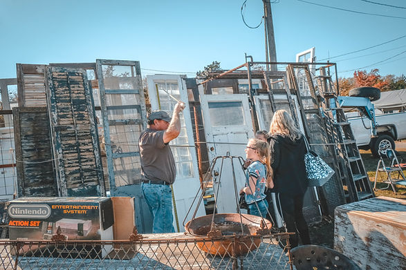 A vendor talking to a family of three in his outdoor lot shop selling antique doors.