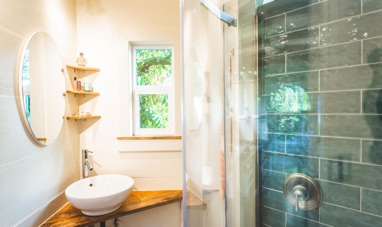 Paradise Tiny Homes
Ellie K Design
Big Island
Oahu, Maui, Kauai, Hawaii luxury homes, real estate, hawaii living, moving to hawaii, hawaii style interior design, condos, portable, modular, Accessory Trailer Unit
As you come into the bathroom and open the obscured glass pocket door, you come smoothly past the curved sliding glass door of the shower. To your left, in the corner, the white vessel sink sits atop a triangular cut mango slab tucked neatly against both walls with small triangle shelving above to match. A frameless oval mirror hangs on the wall 90 degrees from the open bathroom window reflecting light back on it's subject. 