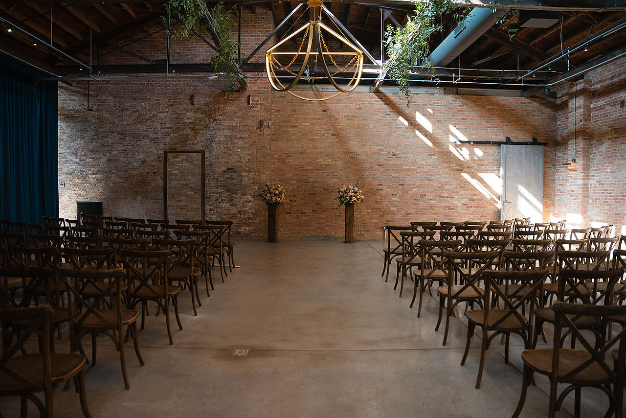 Industrial wedding ceremony setup with wooden chairs, floral pillars, and exposed brick at Wildman BT in Chicago.