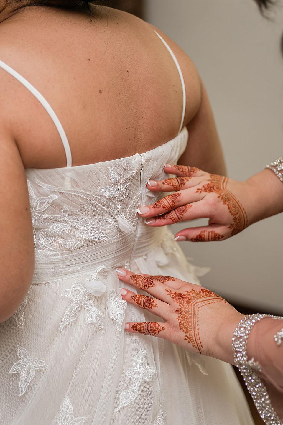 Bride's sister zips up her wedding dress with traditional henna on her hands.