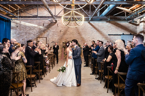Newly married couple kissing in aisle surrounded by cheering guests at Wildman BT Chicago wedding.