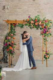 Bride and groom share kiss beneath floral chuppah.