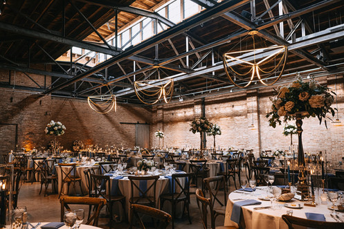 Romantic industrial wedding reception setup at Wildman BT with candlelight, florals, and modern chandeliers.
