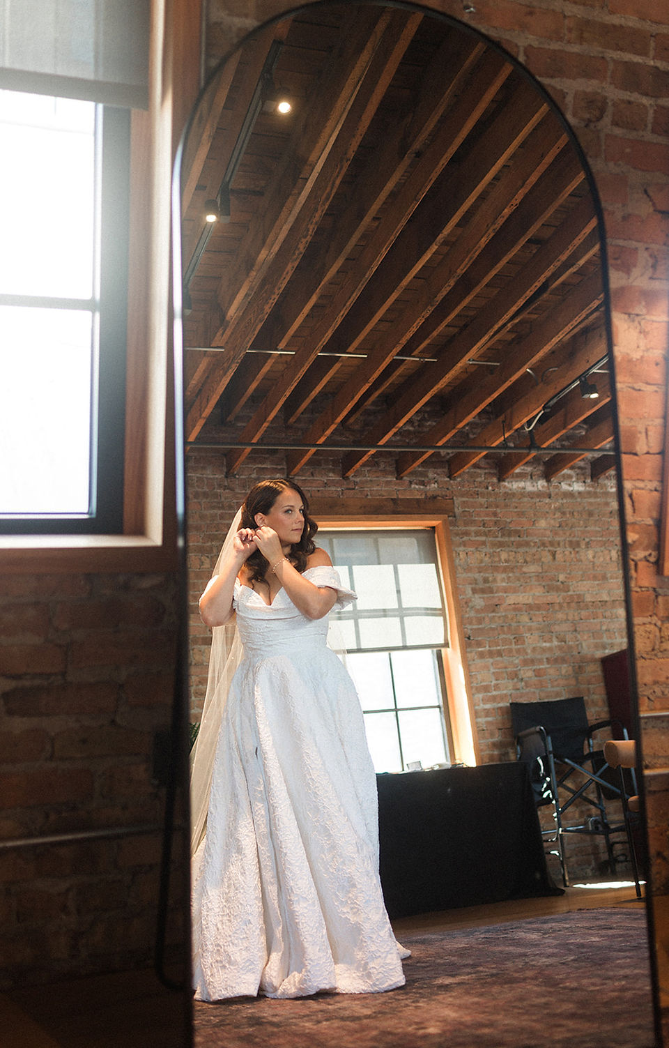 Bride puts earrings on in bridal suite mirror.