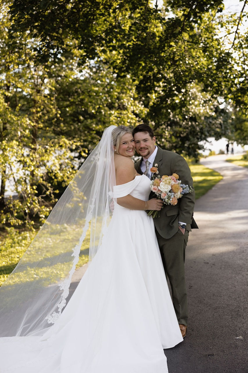 Newlywed couple pose on path surrounded by greenery.