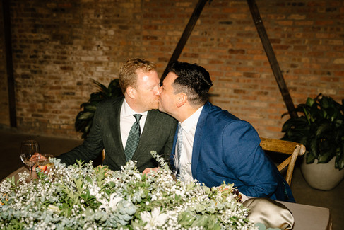 Grooms kiss at head table.