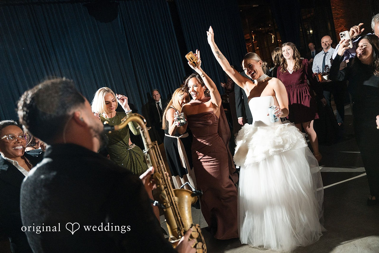 Bride dancing with friends under warm reception lighting at modern indoor wedding venue.