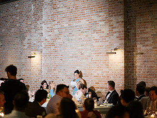 Bridesmaid giving heartfelt wedding toast at brick wall reception venue.