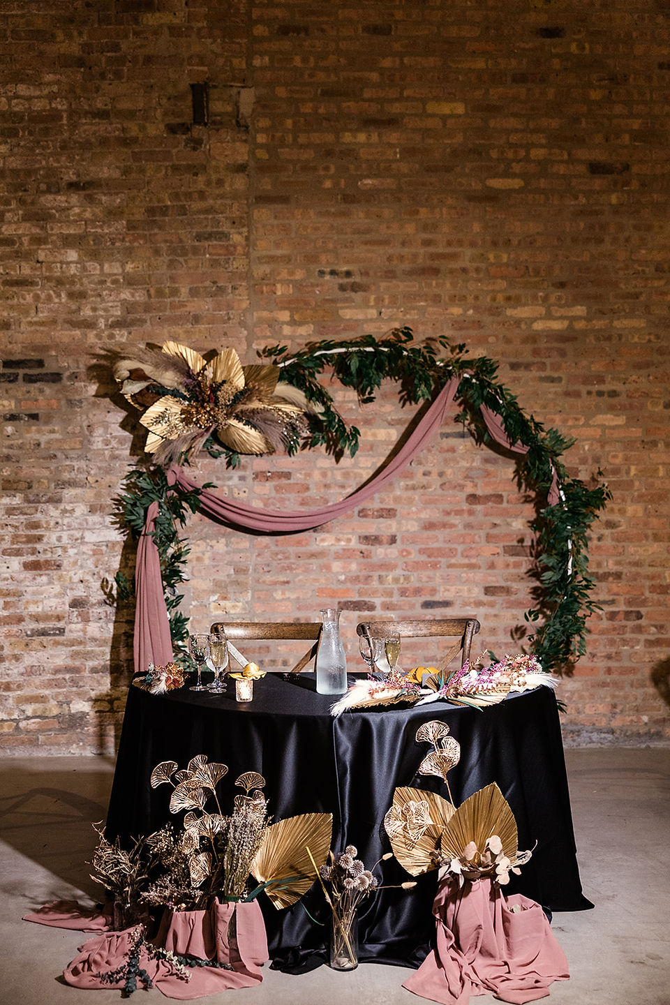 Chic sweetheart table with greenery arch and black and gold decor at industrial Chicago wedding venue.