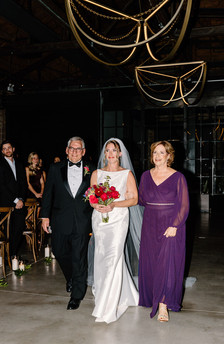 Bride walking down aisle with parents holding bouquet in modern industrial Chicago venue.