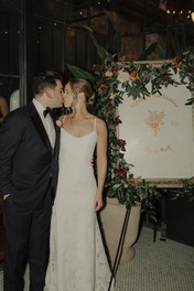 Newlyweds kiss by welcome sign.