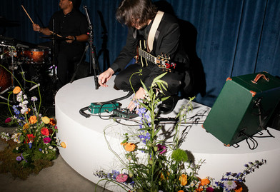 Guitarist on platform surrounded by bright florals.