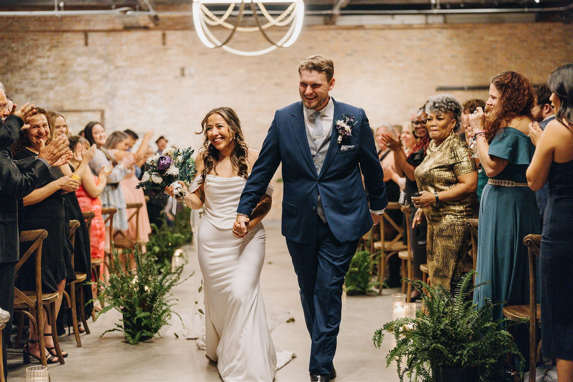 Newlyweds exit ceremony at industrial venue.