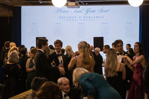 Wedding reception seating chart display with guests mingling in elegant indoor venue.