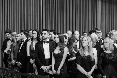 Wedding guests seated during ceremony, black and white candid emotional moment.