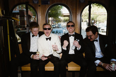 Groom and groomsmen in tuxedos celebrating on trolley ride to Chicago wedding venue.