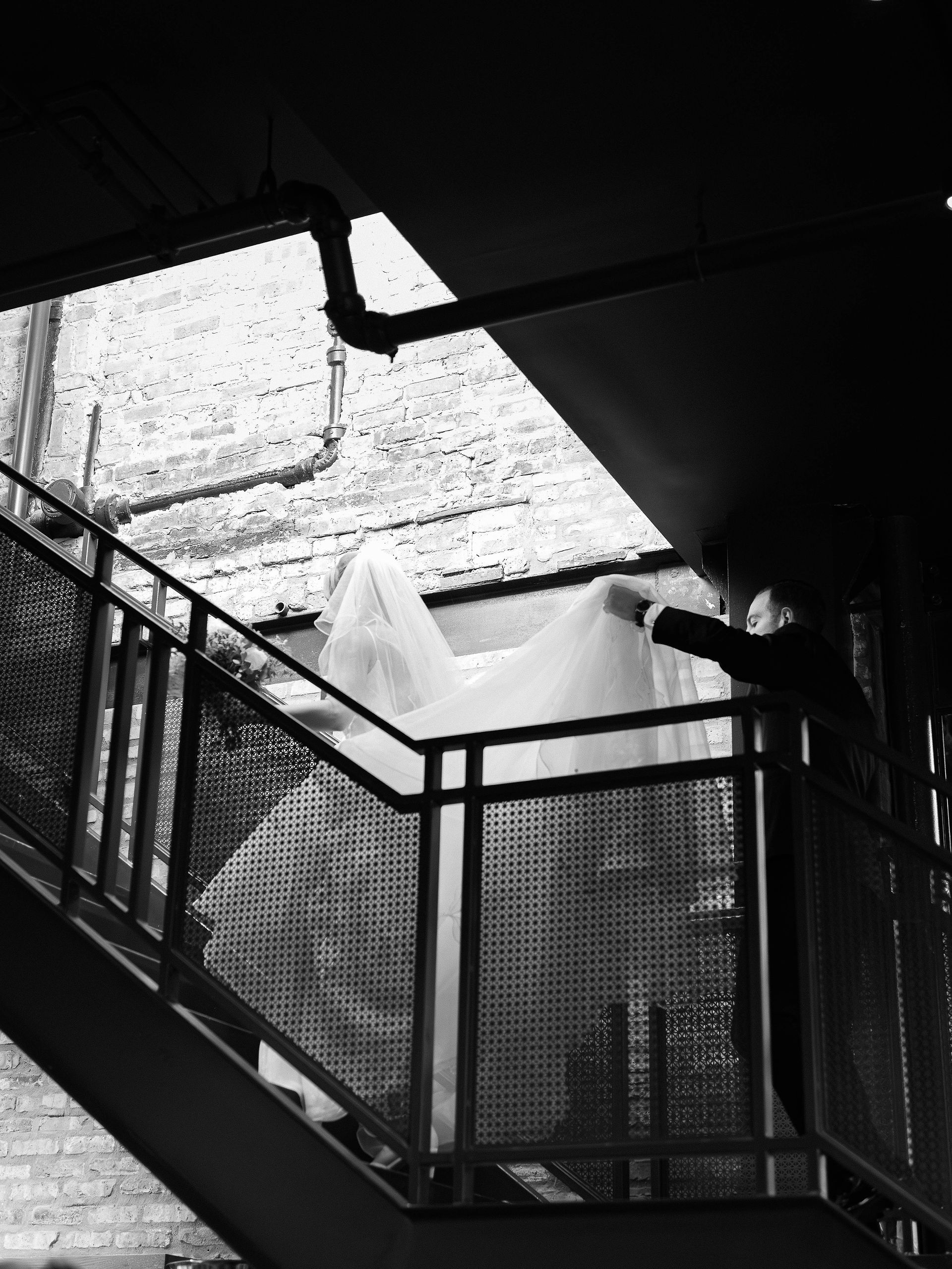 Black and white candid of bride walking up industrial staircase with veil and gown.