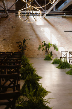 Chicago wedding ceremony with chandeliers, lush greenery, natural lighting, and exposed brick.