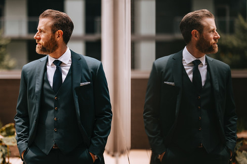 Stylish groom in emerald green suit posing with reflection before Chicago wedding.