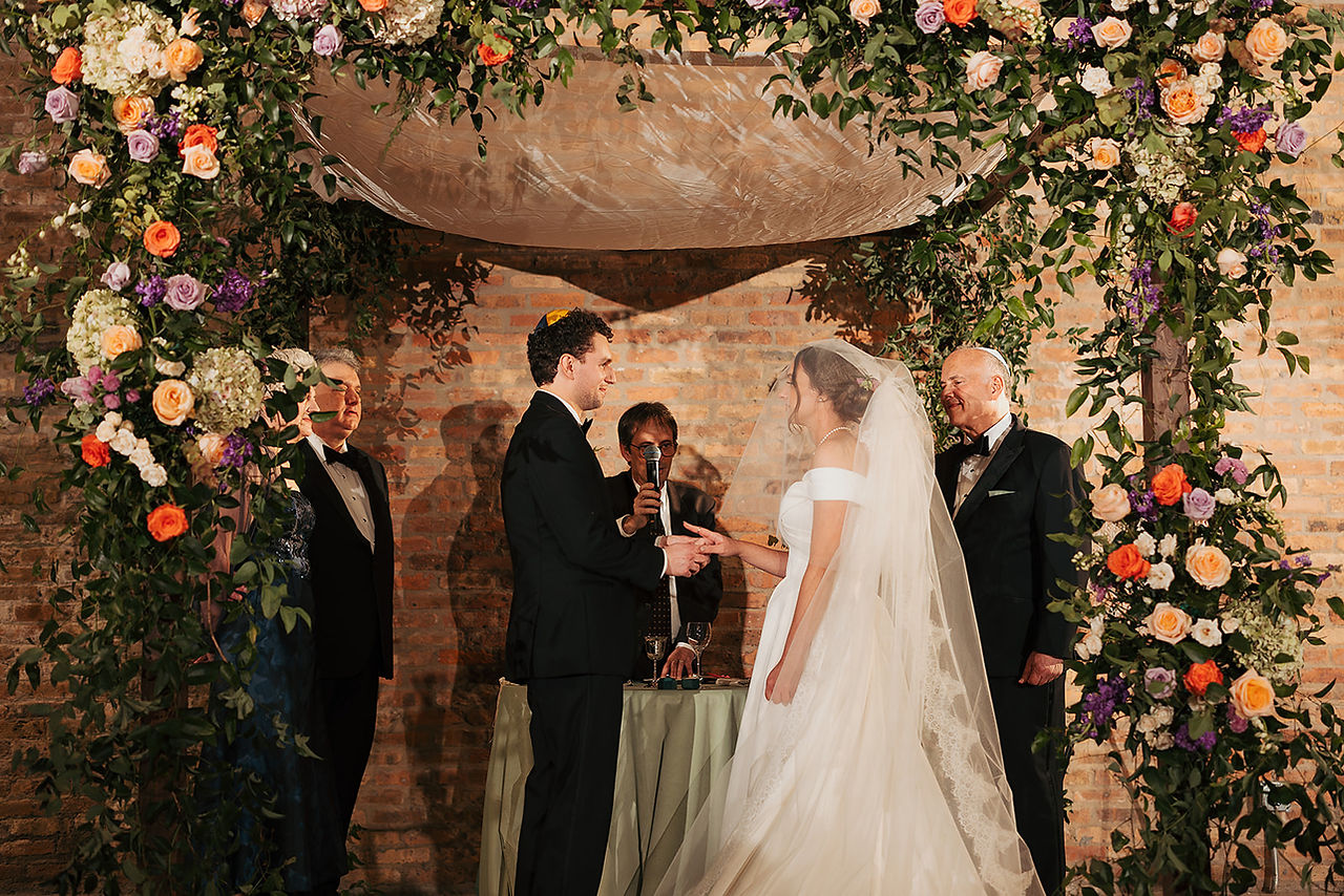 Jewish wedding ceremony under floral chuppah with bride and groom exchanging rings at Wildman BT.