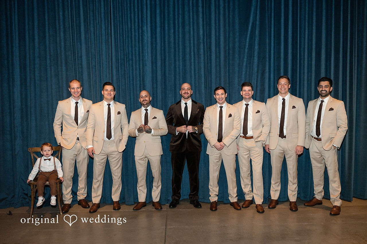 Groom with groomsmen in beige suits posing for formal indoor wedding party portrait.