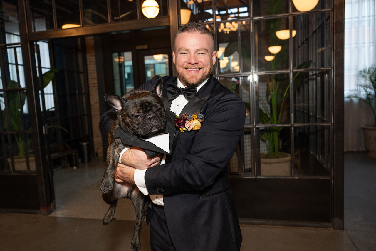 Groom poses with dog in industrial venue.
