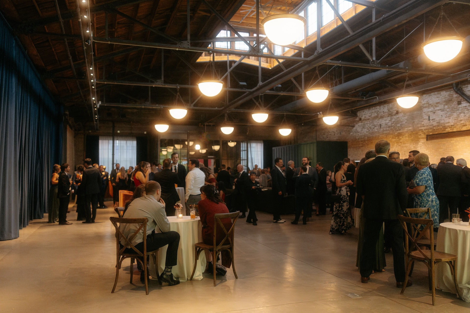 Cocktail hour guests mingling beneath pennant lighting in industrial Chicago wedding venue.