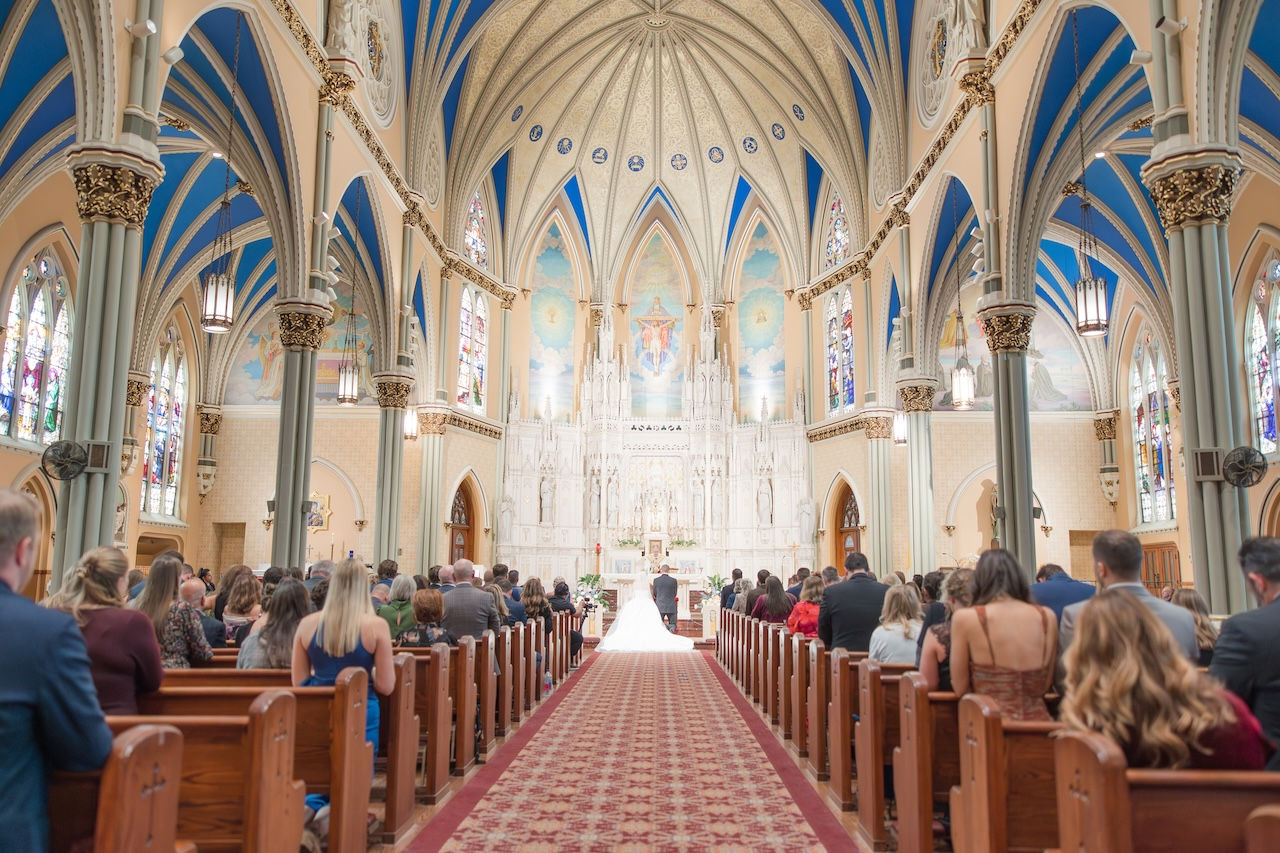 Catholic wedding ceremony inside ornate church with bride and groom at altar.