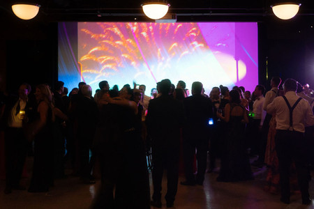 Guests dance in front of projection wall with fireworks in industrial Chicago venue. 