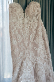 Lace covered wedding dress hangs in hotel room.