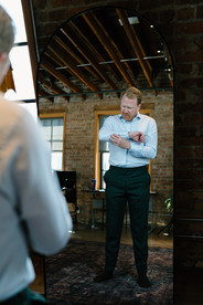 Groom fastens cuffs in mirror.