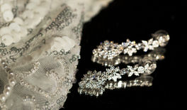 Earrings rests on a mirror, beside a delicate white veil