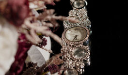A watch lies still on a mirror, framed by flowers