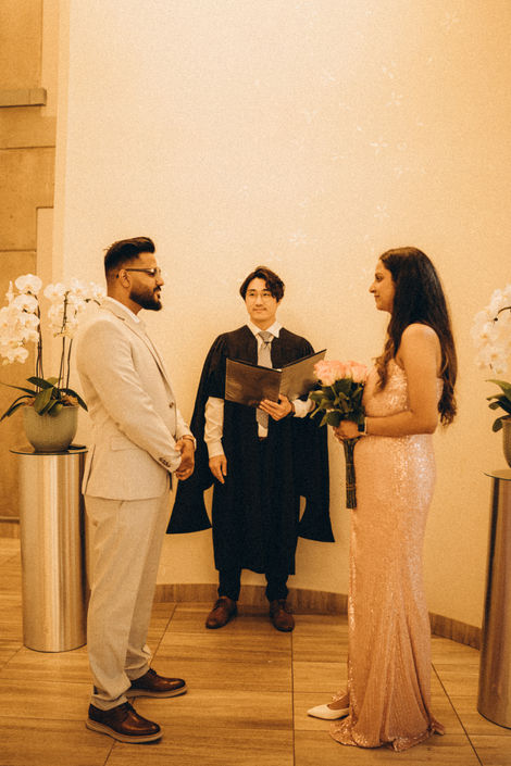 a man in a graduation cap and gown stands between a bride and groom