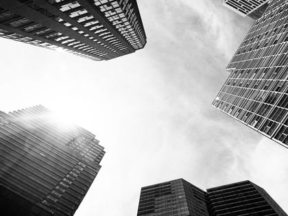 a black and white photo of tall buildings with the sun shining through the windows
