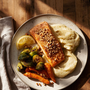 Een stijlvol bord met een stukje zalm met notenkorst, geserveerd met romige aardappelpuree, geroosterde spruitjes en worteltjes. Er ligt een partje citroen naast op het bord. Het tafereel is vastgelegd in warm natuurlijk licht op een houten tafel, met een linnen servet in zachte beige tinten.