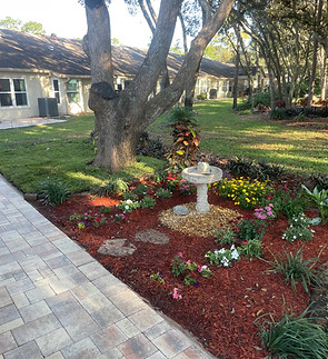 A water fountain with nice flowers laid around it and red mulch