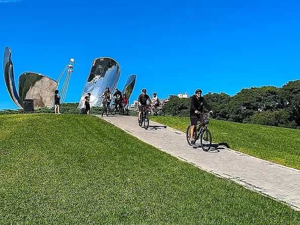 Biker Street cycling group riding through Bosques de Palermo park with the Floralis Genérica sculpture visible in the background, Buenos Aires