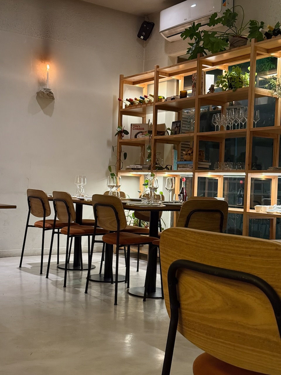 Interior of Alcanfor restaurant in Villa Crespo, Buenos Aires, showing candlelit tables, wooden shelves, and minimalist decor.