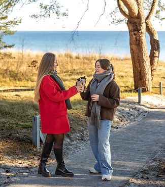 two-women-drinking-hot-coffee-from-thermos-seashore-nature-sea-quay.jpg