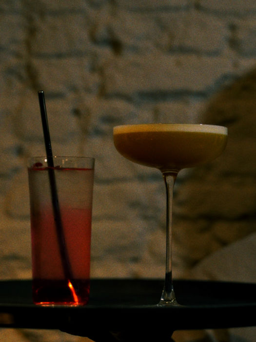 Two cocktails on a tray against a brick wall background