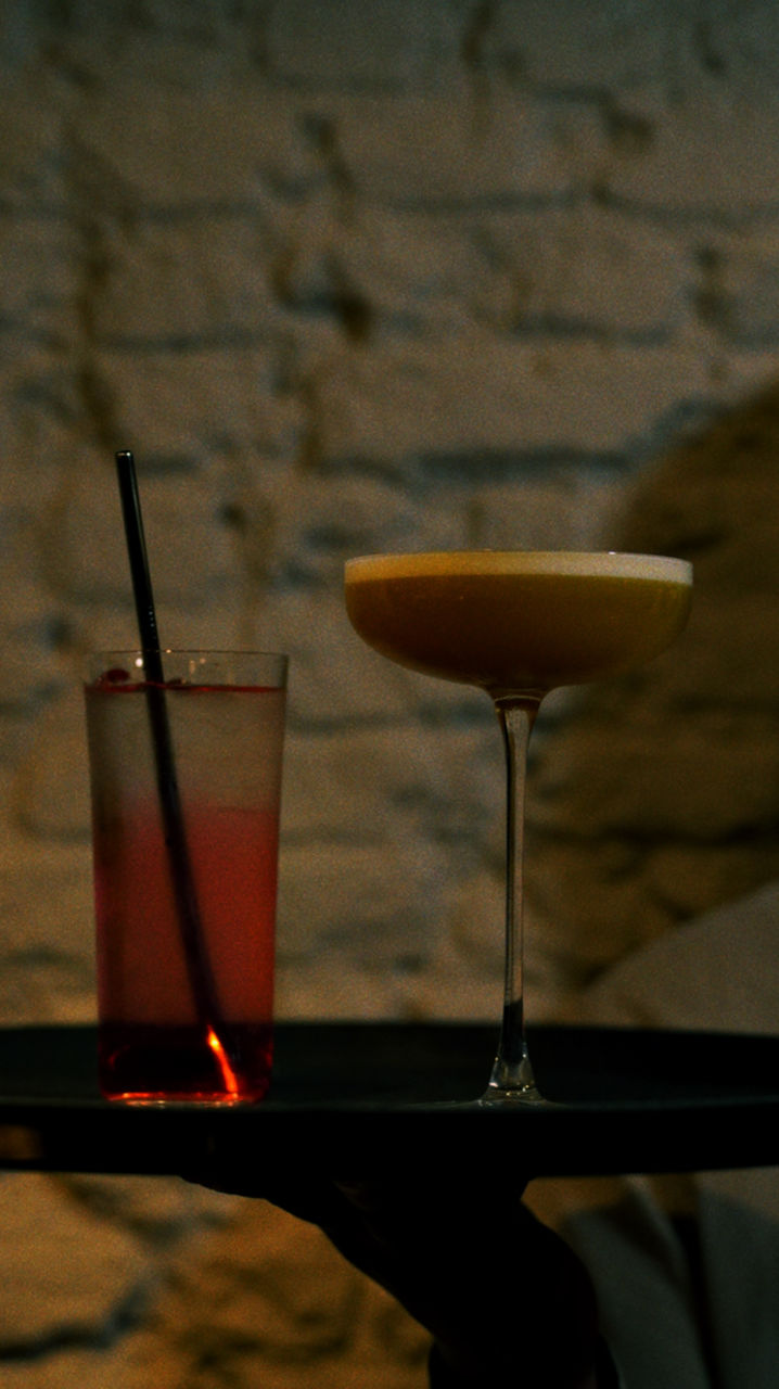 Two cocktails on a tray against a brick wall background