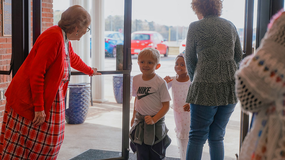 Children enter building, Nike shirt visible. Woman opens door. Serve. Church entrance setting.