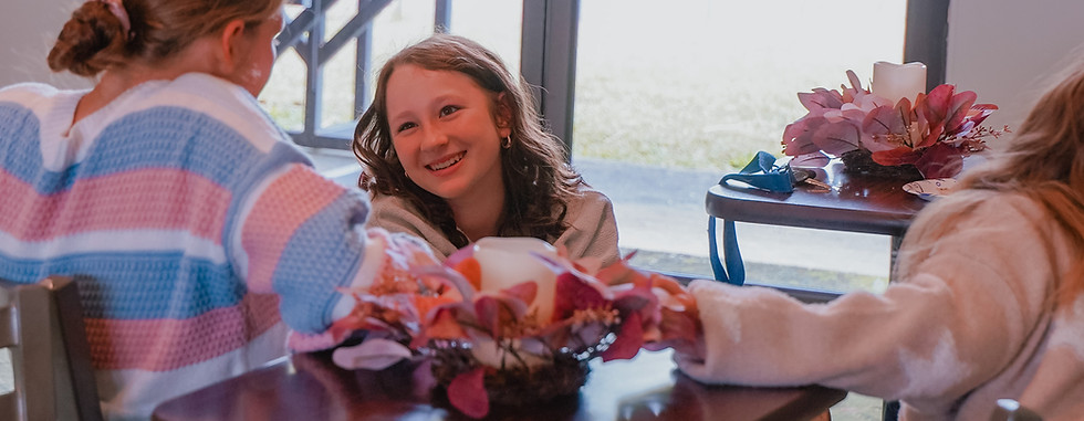 Three young girls laughing together at a table with flowers. Grace Fellowship Madison