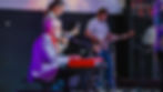 Band playing on stage with keyboard, guitars, and microphones in dim lighting.