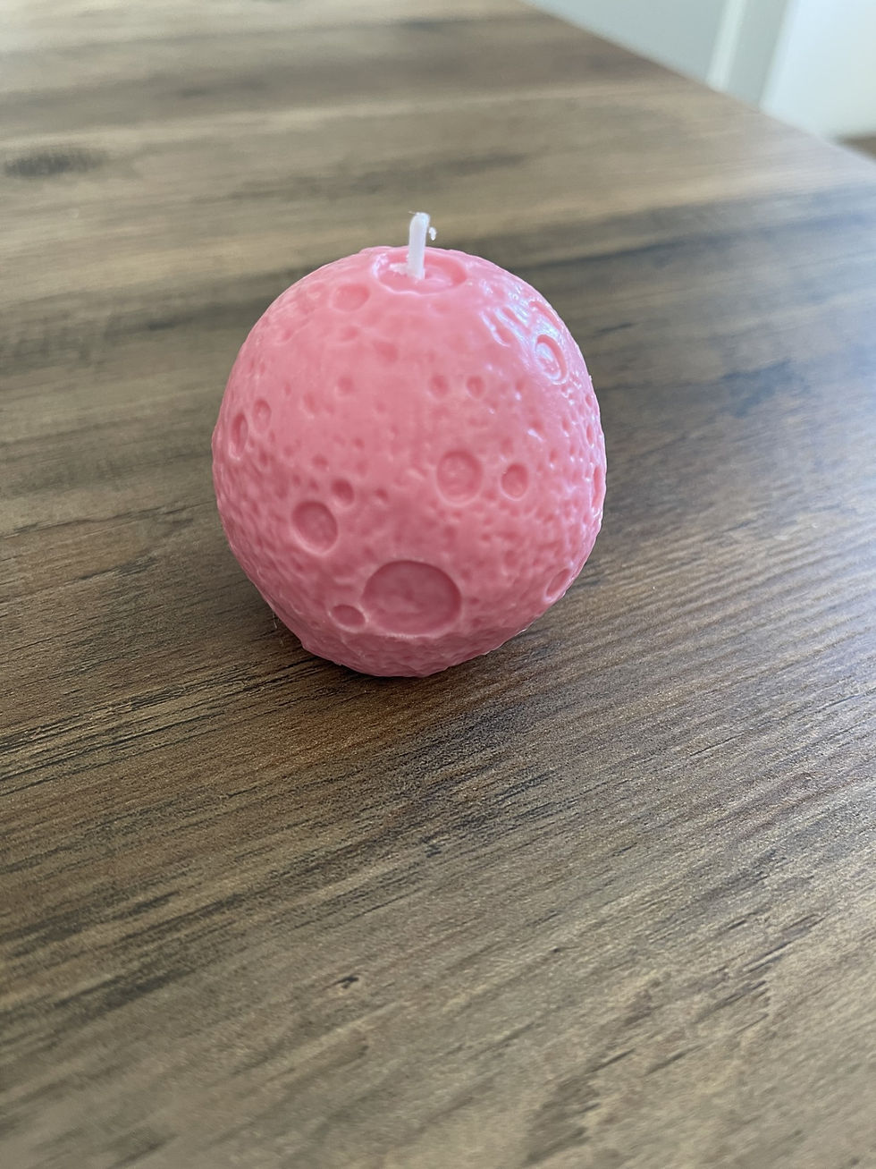Bougie rose en forme de lune, détails des cratères, sur une table en bois.