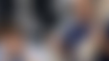 Quiropráctico explicando radiografías espinales con líneas de análisis tipo Gonstead en un monitor digital, mientras sostiene un modelo de columna y un goniómetro; el paciente se masajea las sienes mostrando sobrecarga mental por exceso de explicación.