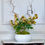 Thumbnail: yellow hellebores in white ceramic planter with contorted hazel branches and green moss - whispering lily