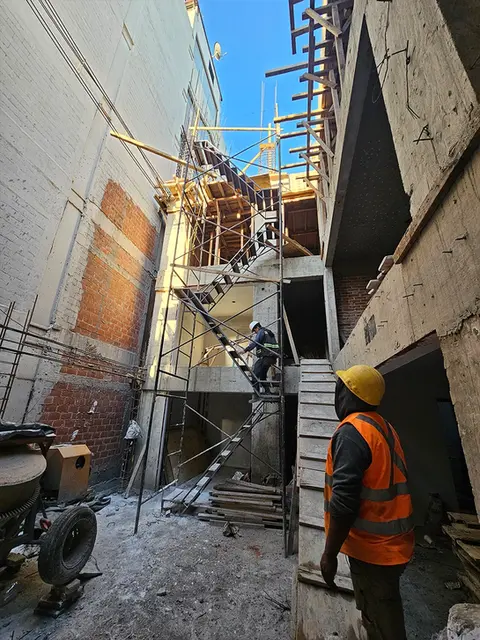 Fase de construcción estructural de un desarrollo residencial, mostrando el uso de andamios, vigas de madera y personal de obra trabajando en los niveles superiores.